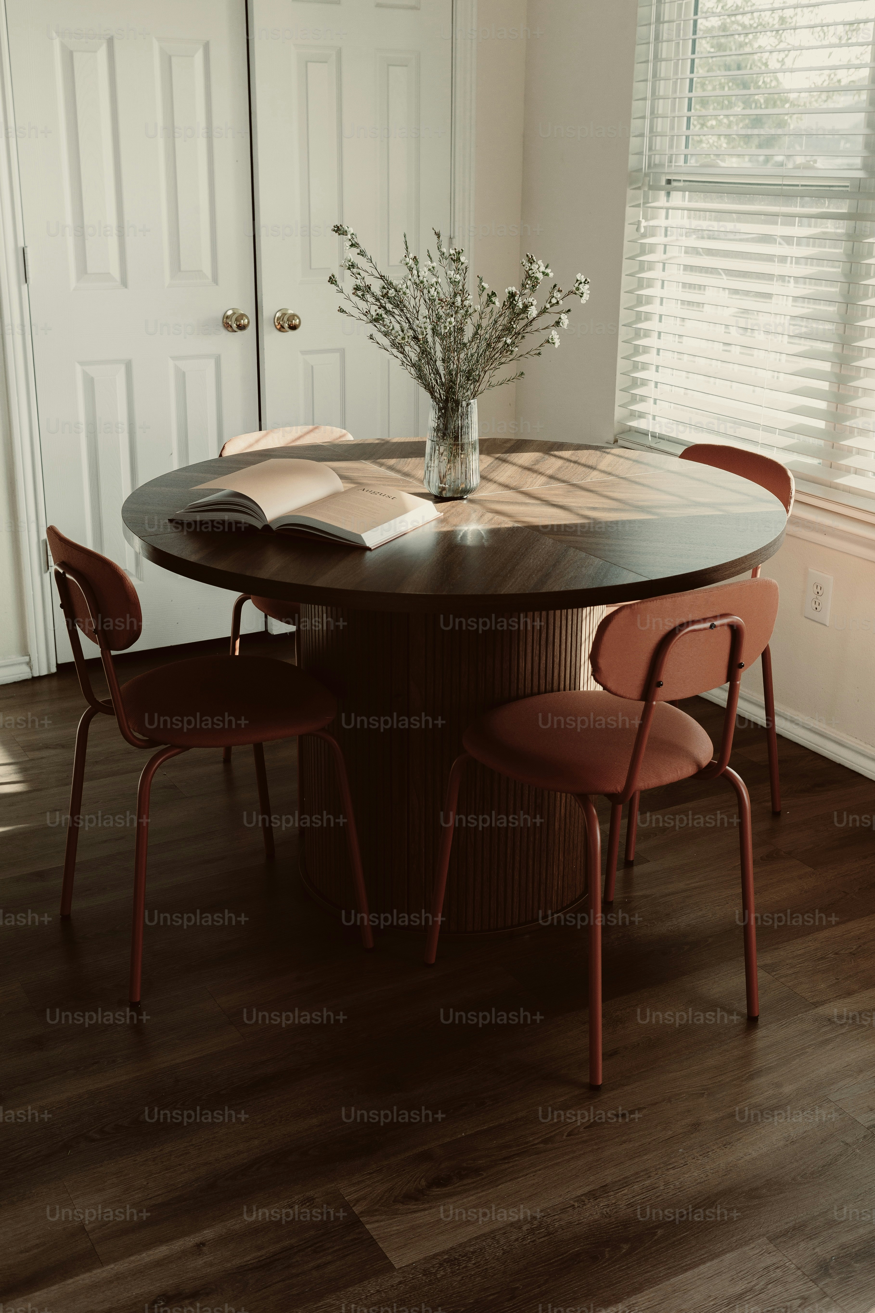 Round dining table with red chairs and dried flowers.